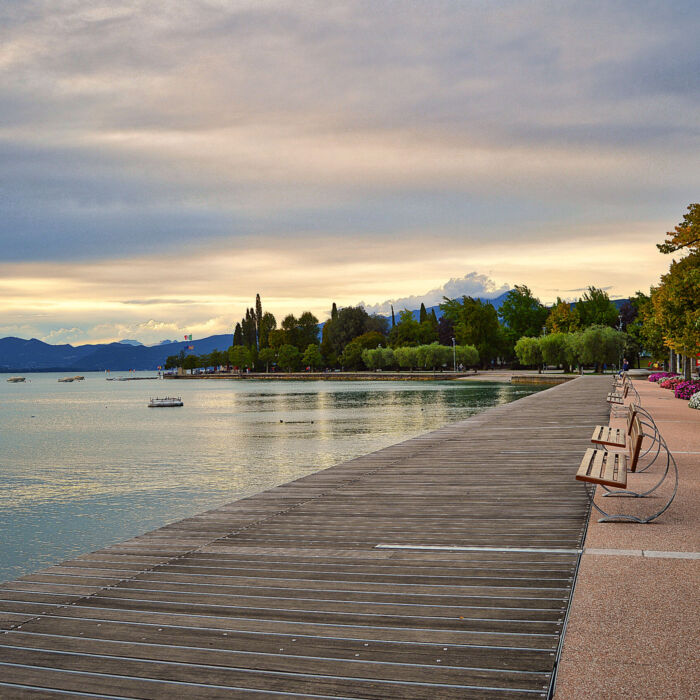 promenade pier of Bardolino, lake Garda with benches, flowers, trees, water and dramatic evening sky